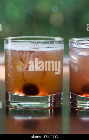 Two iced cocktails with cherries in short glasses with foliage in the background Stock Photo