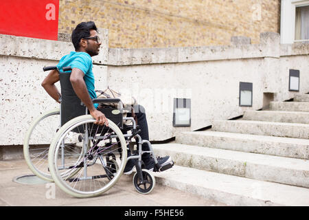 disabled man in a wheelchair waiting at the bottom of steps Stock Photo