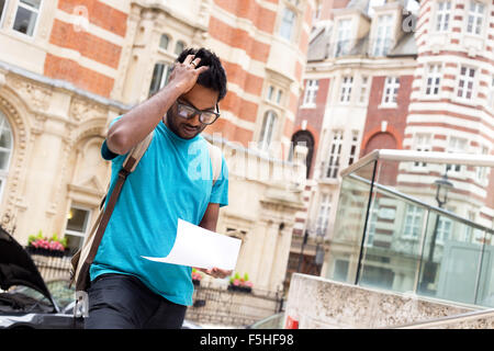 worried young man reading a letter in the street Stock Photo
