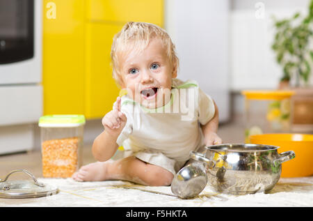 Playful child boy with kitchenware and foodstuffs on floor in kitchen Stock Photo