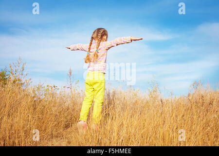 Little girl in bright clothes standing against the sky Stock Photo