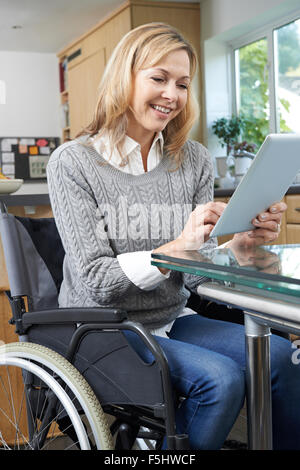 Disabled Woman In Wheelchair Using Digital Tablet At Home Stock Photo