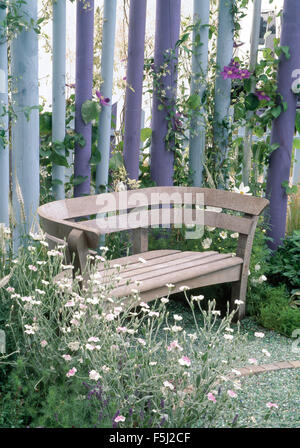 White lychnis beside a wooden seat on a small patio against pale blue and purple fencing  in town garden Stock Photo