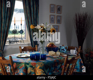 Vase of summer flowers on table set for lunch with colourful cloth in nineties dining room Stock Photo