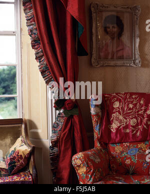 Nineties living room with a red floral armchair beside window with red silk curtains with ruched trimming Stock Photo