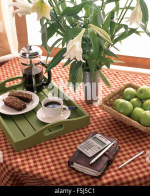 Vase of white lilies and Filofax with a calculator on a table with a cafetiere and cup of coffee on a green tray