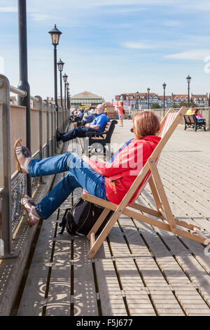 Woman sitting on a deck chair relaxing with her feet up on Skegness pier, Lincolnshire, England, UK Stock Photo