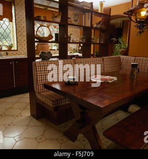 Checked cushions on banquette seating at a dark wood table in a seventies kitchen diner Stock Photo