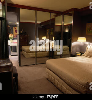 Mirrored doors on fitted wardrobe in an eighties bedroom with a fitted bed cover on the bed Stock Photo