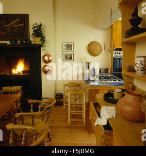 Rush seated wooden stools at tiled breakfast bar in a seventies kitchen with a lighted fire in the fireplace Stock Photo