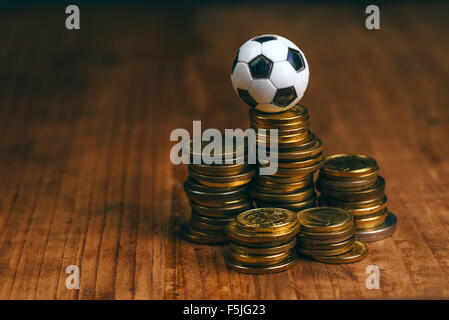 Soccer bet concept with small football on top of coin stack, making money by predicting sport results. Stock Photo