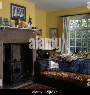 Kelim rug on blue sofa beside fireplace with a small wood burning stove in a yellow nineties living room Stock Photo