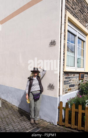 A woman in a hat next to high water (hochwasser) flood markers on a house wall, Enkirch, Mosel river, Rheinland-Pfalz, Germany Stock Photo