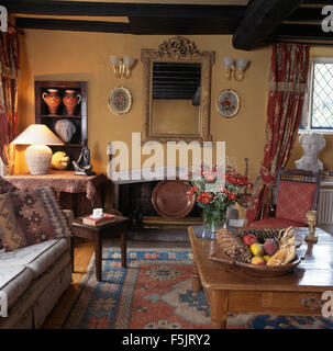 Ornate carved mirror above fireplace recess in a country sitting room with a lighted lamp on table in front of alcove shelves Stock Photo