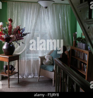 White voile curtains on nineties landing with a large floral arrangement on a side table Stock Photo