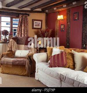 Patterned throws on armchair in dark nineties cottage living room with a white sofa piled with cushions Stock Photo