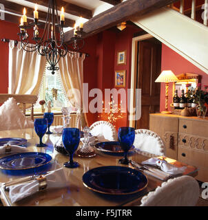 Table set for lunch with blue and wineglasses and plates in a red nineties cottage dining room with cream drapes on window Stock Photo