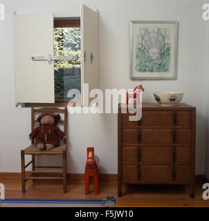 Arts+Crafts chest-of drawers in bedroom with ladder-back chair below window with simple white shutters Stock Photo