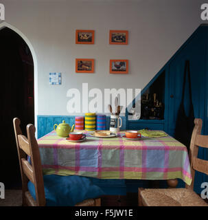 Pink, green and blue checked cloth on table with colorful crockery in a nineties economy dining room Stock Photo