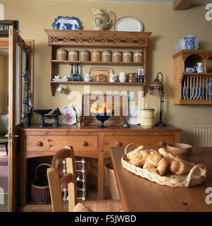 Basket of croissants on table in a cottage kitchen dining room with pine shelves above a pine dresser Stock Photo