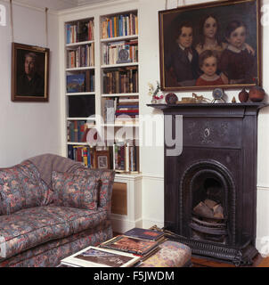 Oil painting above small cast iron fireplace i  a nineties living room with built in bookcase and a patterned sofa Stock Photo