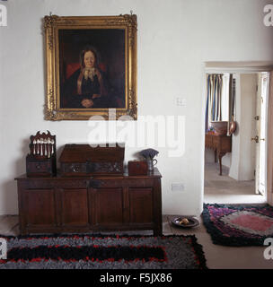 Oil portrait in gilt frame above antique oak chest with a vintage silver spoon rack in country hall with rag rugs on floor Stock Photo