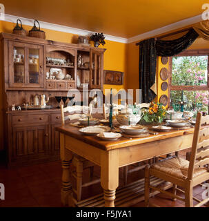 Ladder back chairs at pine table set for lunch in a yellow nineties dining room with an wooden dresser Stock Photo