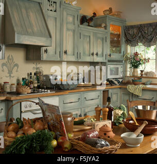 Table piled with cookery ingredients and utensils in a cluttered nineties kitchen with painted doors on fitted units Stock Photo
