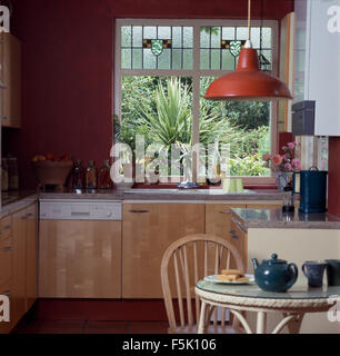 Stained glass panels in window above sink and dishwasher in kitchen with red enamel light fitting Stock Photo