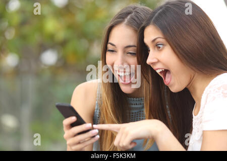 Euphoric friends watching videos on a smartphone and pointing at screen surprised Stock Photo
