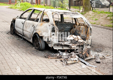 Burnt car back in arson fire, white car wreck at the pavement in Poland, spoilt empty car in fire accident, charred vehicle junk Stock Photo