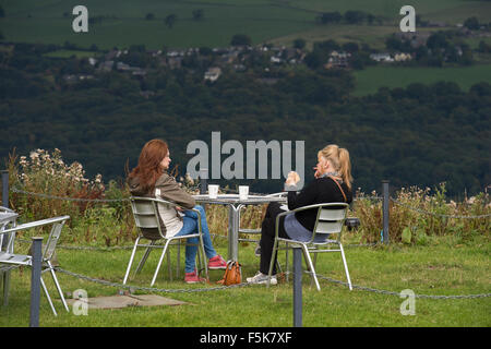 2 women friends sitting outside, eating & chatting at Cow & Calf Rock café, Ilkley, Yorkshire, UK - scenic spot with panoramic view over the valley. Stock Photo