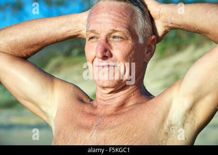 Head and shoulder portrait of a mature aged man smiling with sand dunes and tree in the background Stock Photo