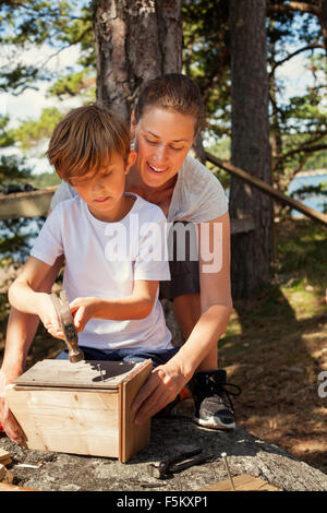 Sweden, Uppland, Runmaro, Barrskar, Mother helping son (6-7) to build birdhouse
