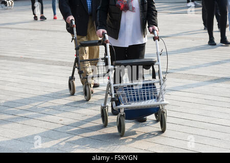 An elderly couple is walking on the street with their walking frames Stock Photo