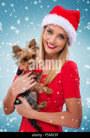 Beautiful santa woman, holding  santa yorkshite terrier, snowfall background Stock Photo