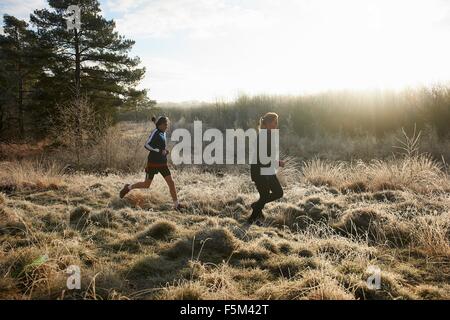 Side view of mother and sons running on frosty grassland Stock Photo