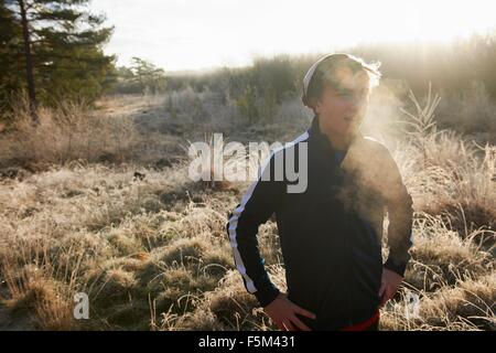 Teenage boy on frosty grassland, visible breath, hands on hips looking away Stock Photo