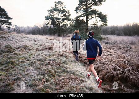 Rear view of mother and son running on frosty grassland Stock Photo