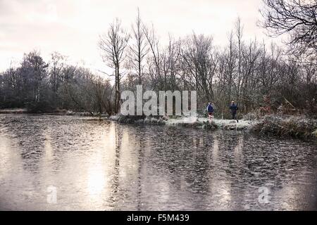 View across icy lake of mother and son running together Stock Photo