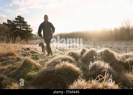Front view of mature woman walking dog on grassland looking away Stock Photo