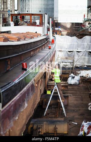 Worker on step ladder checking boat in shipyard workshop Stock Photo