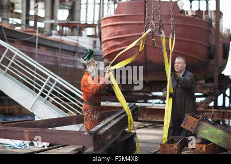 Workers using winch for girders in shipyard workshop Stock Photo