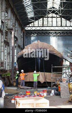 Three workers wrapping boat in shipyard Stock Photo
