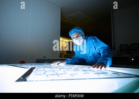 Male worker inspecting flex circuit on lightbox in flexible electronics factory clean room Stock Photo