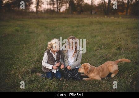 Two young girls sitting in field with pet dog Stock Photo