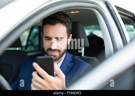 Young businessman reading smartphone texts in car Stock Photo