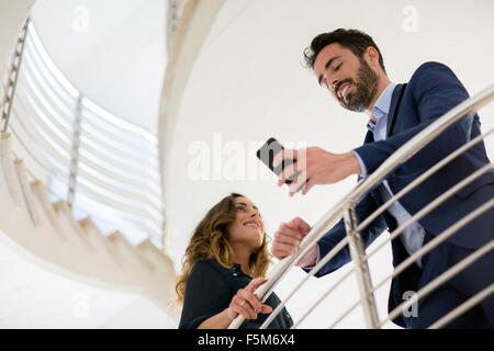 Young businessman reading smartphone texts on office stairway Stock Photo