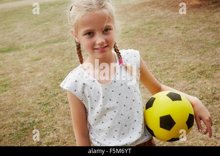 High angle view of girl with pigtails holding soccer ball looking at camera smiling Stock Photo