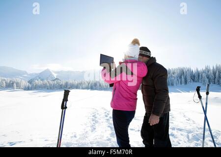 Rear view senior couple snowy landscape digital tablet take photograph mountain range Sattelbergalm Tyrol Austria Stock Photo